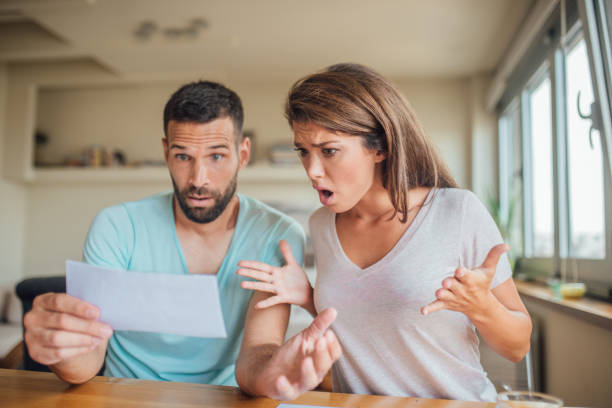 shocked young couple looking at their bills at home - shocked couple stock pictures, royalty-free photos & images