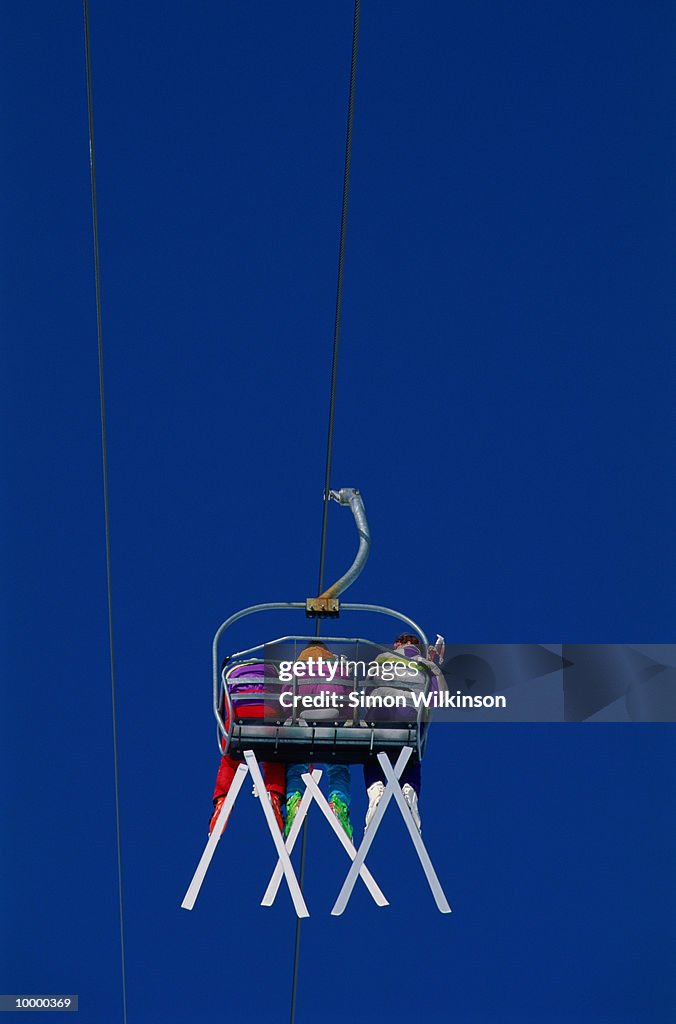 BACKVIEW OF THREE SKIERS ON CHAIR LIFT