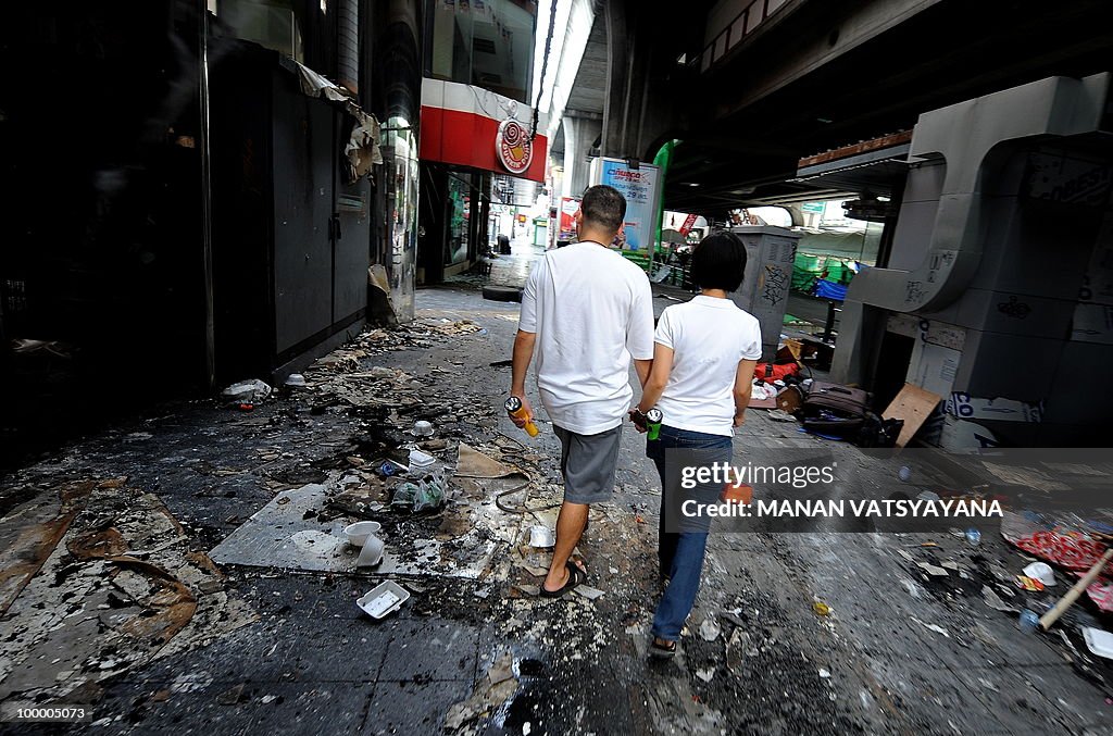 A Thai couple walks past burnt shops in