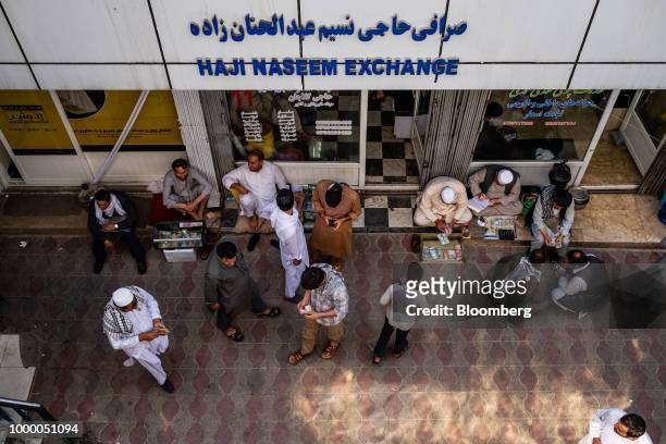 Money changers sit behind bundles of banknotes outside a foreign exchange store at the money exchange market in Kabul, Afghanistan, on Thursday, July...