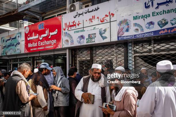 Men carrying bundles of cash stand outside foreign exchange stores at the money exchange market in Kabul, Afghanistan, on Thursday, July 12, 2018....
