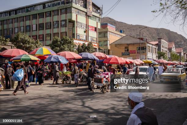 Worker pushes a cart past shoppers and stalls in a street market in Kabul, Afghanistan, on Thursday, July 12, 2018. U.S President Donald last year...