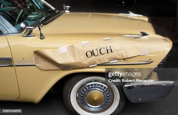 An 'Ouch' sign covers damage from a recent accident on a 1950s Plymouth on display at a classic car show in Santa Fe, New Mexico.