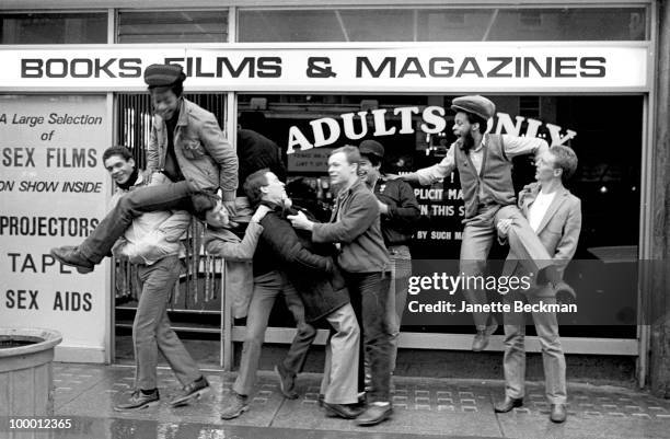 Portrait of British reggae group UB40 as they clown about in front of a sex shop), Brimingham, England, 1981. Pictured are band members Ali Cambell,...