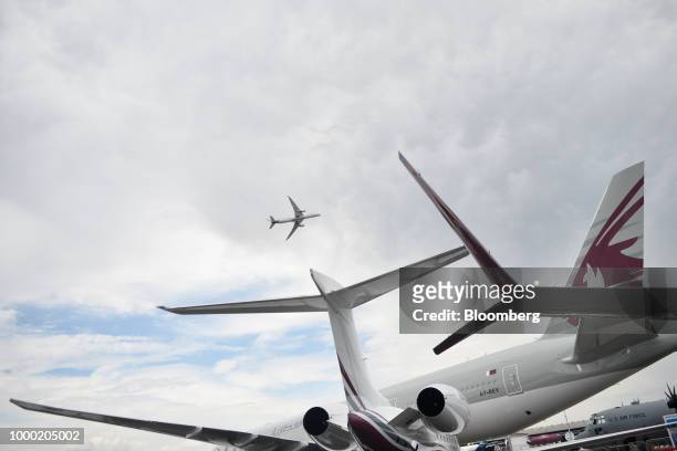 An aircraft flies above tail fins of a plane parked in the static display area on the opening day of the Farnborough International Airshow 2018 in...