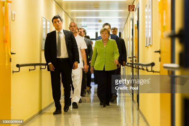German Chancellor Angela Merkel walks with Ferdi Cebi , a caregiver at the St. Johannesstift senior care facility, during a visit on July 16, 2018 in...