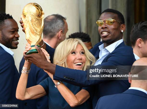 French President Emmanuel Macron's wife Brigitte Macron holds the trophy next to France's midfielder Paul Pogba during a reception at the Elysee...