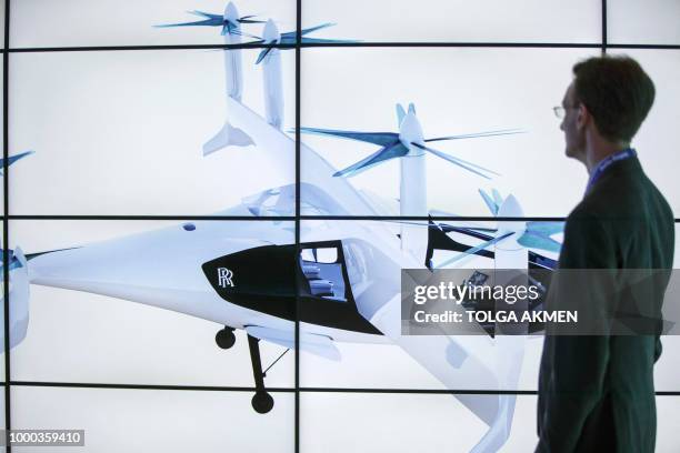 Man poses alongside screens presenting the Rolls-Royce EVTOL air taxi concept during the Farnborough Airshow, south west of London, on July 16, 2018....