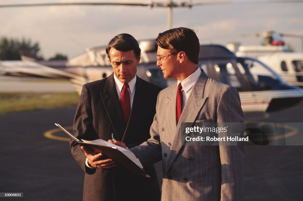 Businessmen signing papers near helicopter