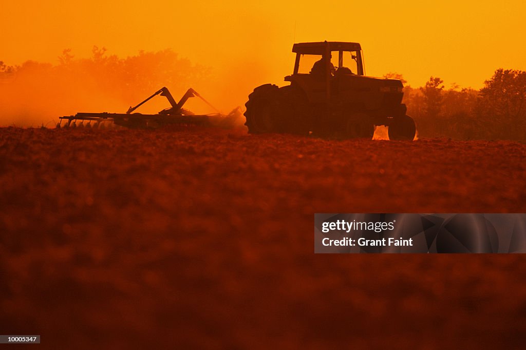 TRACTOR PLOWING FIELD AT SUNSET