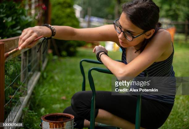 the attractive 15-years-old teenager girl painting the fence at the backyard - 14 15 years girl stock pictures, royalty-free photos & images
