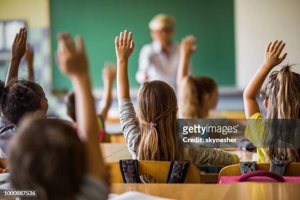 back view of elementary students raising their arms on a class. - learning stock pictures, royalty-free photos & images