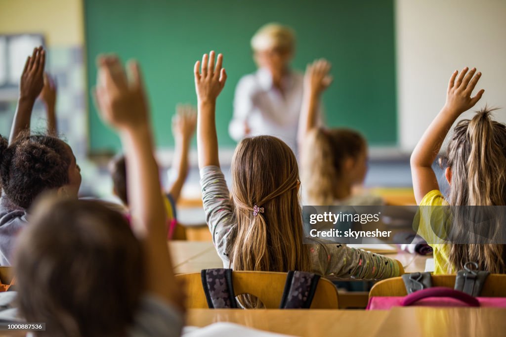 Baksidan på elementära studenter att höja armarna på en klass.