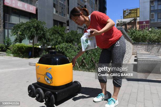 Woman picks up groceries delivered by a Zhen Robotics delivery robot at a residential compound during a demonstration of the robot in Beijing. -...