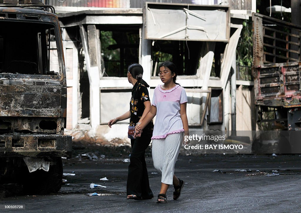 Two women walk past burnt trucks and a p