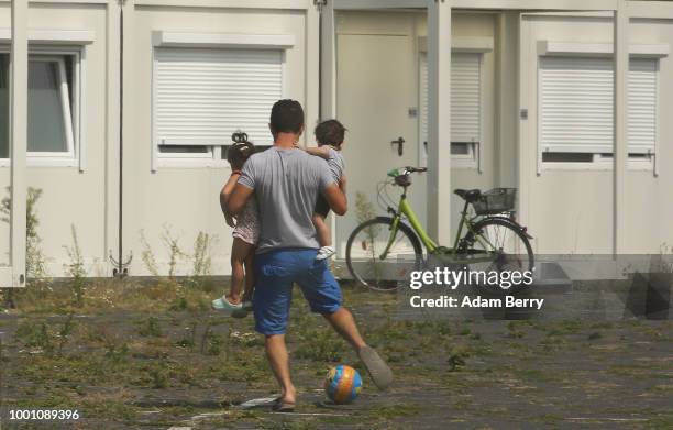 Man kicks a ball while carrying his children inside a temporary refugee reception center at the former Tempelhof airport on July 18, 2018 in Berlin,...