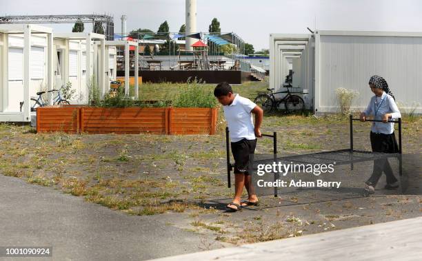 Young asylum seekers carry a bed frame at a temporary refugee reception center at the former Tempelhof airport on July 18, 2018 in Berlin, Germany....