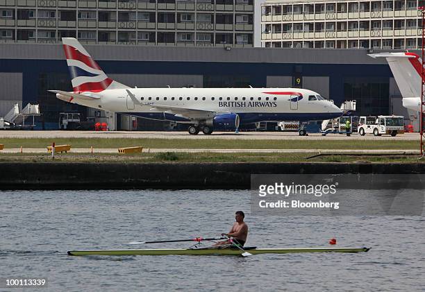 Rower passes a British Airways airplane as it sits on the tarmac at City Airport in London, U.K., on Friday, May 21, 2010. British Airways Plc said...
