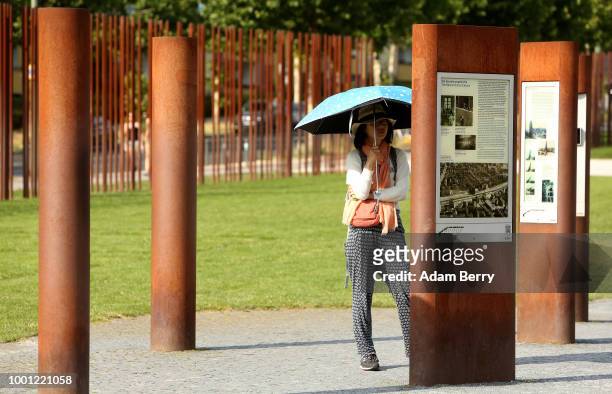 Visitor to the Berlin Wall Memorial exhibition shields herself with an umbrella while reading an information panel on July 18, 2018 in Berlin,...