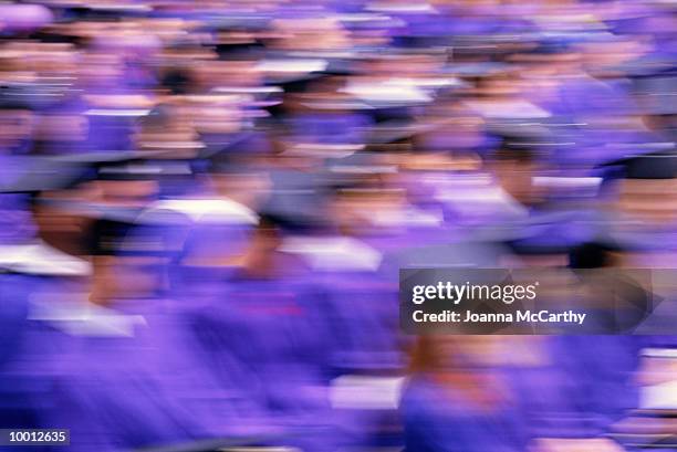seated graduates in caps & gowns in blur - graduation crowd stock-fotos und bilder