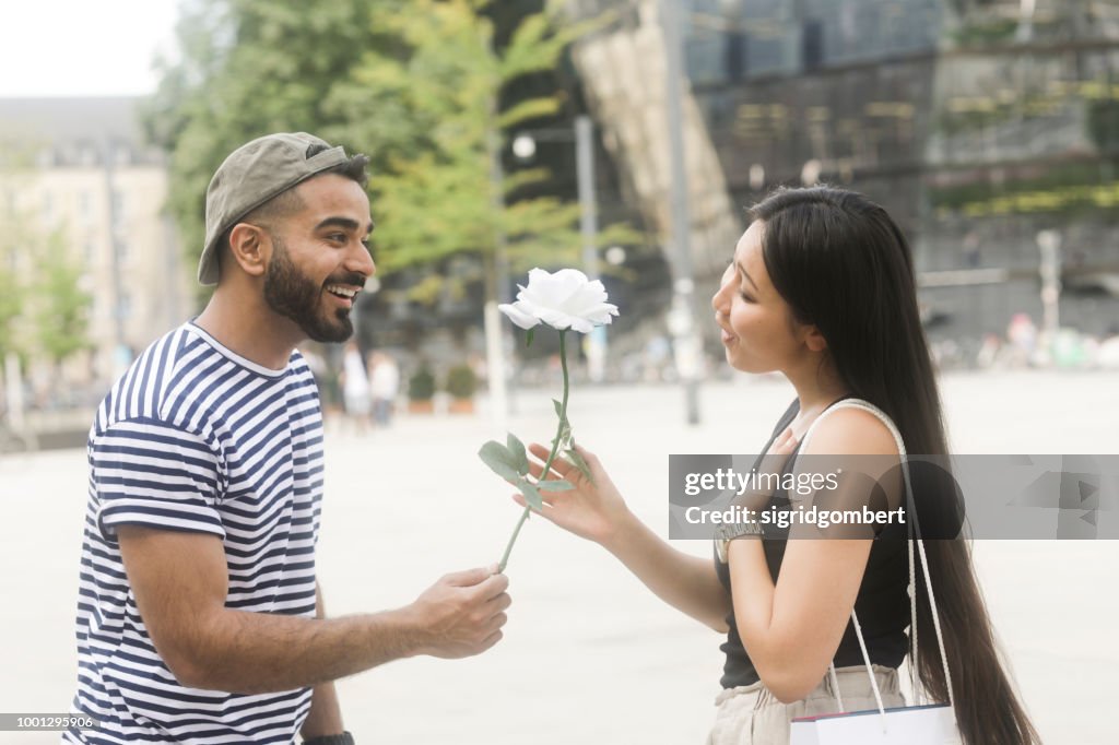 Man standing in city square giving his girlfriend a white rose