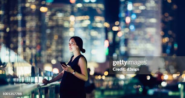 beautiful asian pregnant woman text messaging on smartphone in downtown financial district at night - welvaart stockfoto's en -beelden