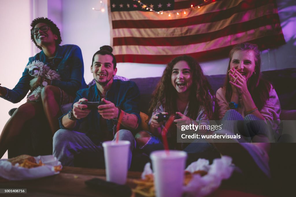 Young multi-ethnic friends eating fast food and playing video games