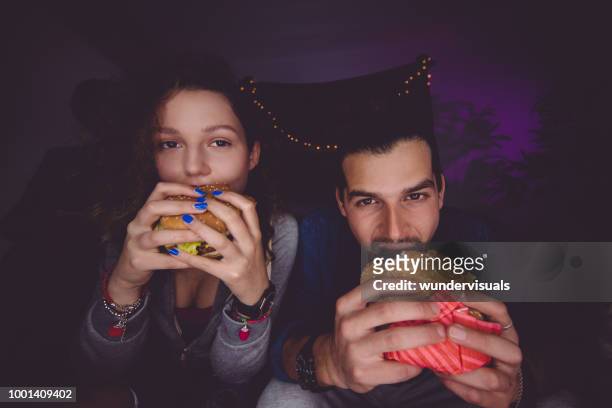 portrait of young man and woman eating hamburgers - college dorm party stock pictures, royalty-free photos & images