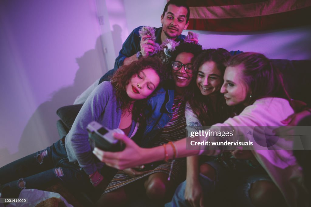 Smiling multi-ethnic friends taking selfie at home with vintage camera