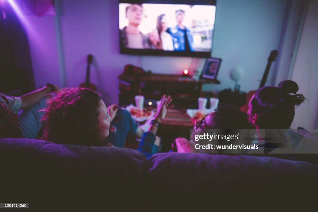 Multi-ethnic teenage friends watching TV together at hangout house