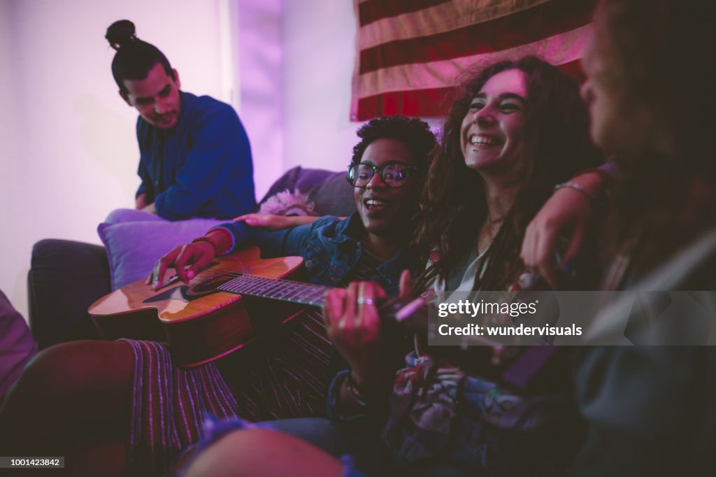 Multi-ethnic hipster friends playing the guitar and singing at home