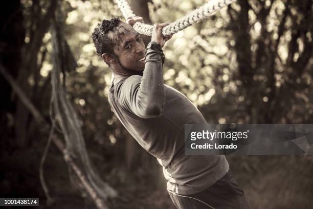 individual non caucasian adult male having sporty fun at a public mud run obstacle course - training camp stock pictures, royalty-free photos & images