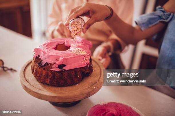 woman adding colorful sprinkles on cake icing - hundreds and thousands stock pictures, royalty-free photos & images