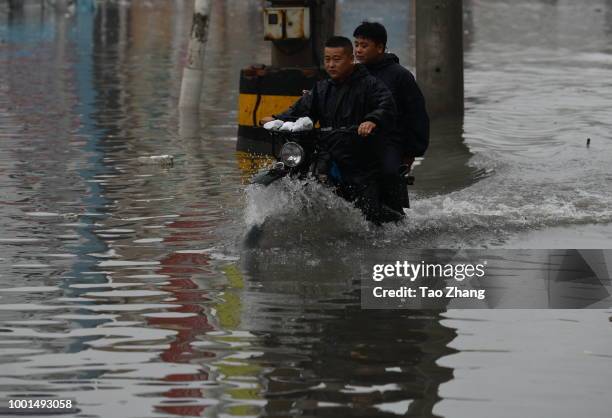 People ride a motor on a flooded street caused by heavy rainstorms in Harbin city, northeast China's Heilongjiang province, 19 July 2018. Rainstorms...