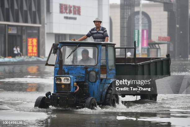 People drive a tractor on a flooded street caused by heavy rainstorms in Harbin city, northeast China's Heilongjiang province, 19 July 2018....
