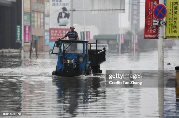 People drive a tractor on a flooded street caused by heavy rainstorms in Harbin city, northeast China's Heilongjiang province, 19 July 2018....