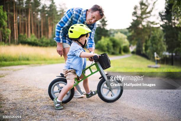 a small toddler boy with his grandfather riding a balance bike outdoors. - fahrrad fahren großeltern mit kind stock-fotos und bilder