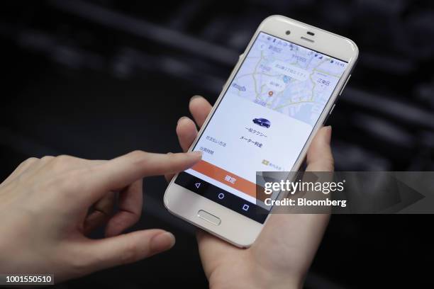 An attendant demonstrates the Didi Chuxing taxi-hailing application on a smartphone for a photograph at the SoftBank World 2018 event in Tokyo,...