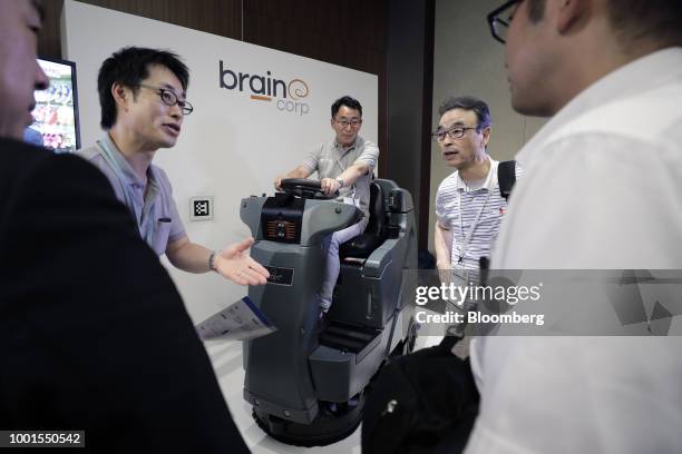 An attendant, center, sits on an International Cleaning Equipment RS26 rider auto scrubber, powered by Brain Corp.'s Brain OS, at the SoftBank World...