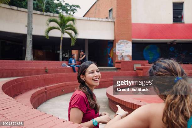 deux amis de femmes hispaniques siégeant ensemble tout en riant, dans une zone urbaine - valle del cauca photos et images de collection