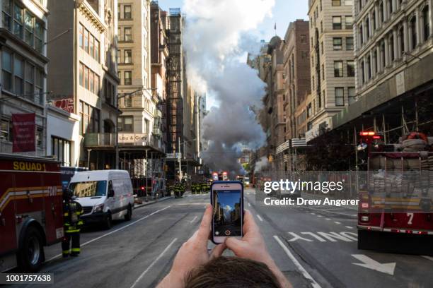 Man takes a photo with his smartphone near the site of a steam pipe explosion on Fifth Avenue near the Flatiron District on July 19, 2018 in New York...