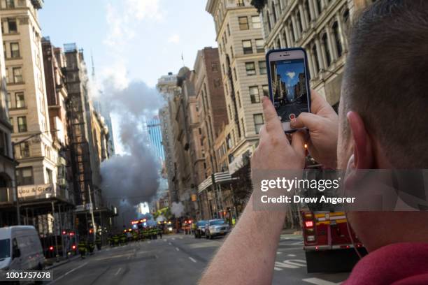 Man takes a photo with his smartphone near the site of a steam pipe explosion on Fifth Avenue near the Flatiron District on July 19, 2018 in New York...