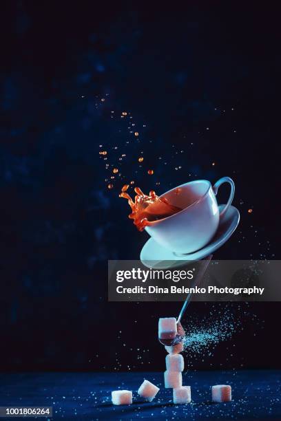 coffee cup with a dynamic splash balancing on a spoon and a stack of sugar cubes. magical levitation drink on a dark background. action food photography - coffee slow motion stock pictures, royalty-free photos & images