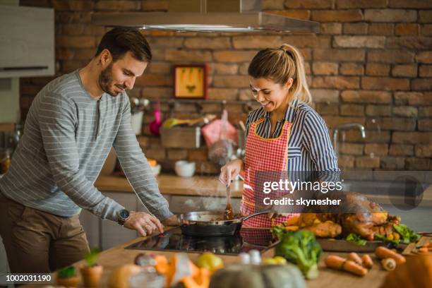 young happy couple cooperating while cooking side dish for thanksgiving dinner. - christmas preparation stock pictures, royalty-free photos & images