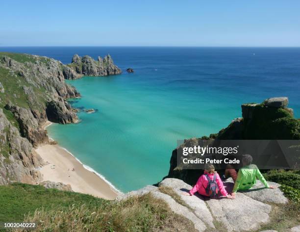 couple sat on clifftop looking down at beach - lands end cornwall stock-fotos und bilder