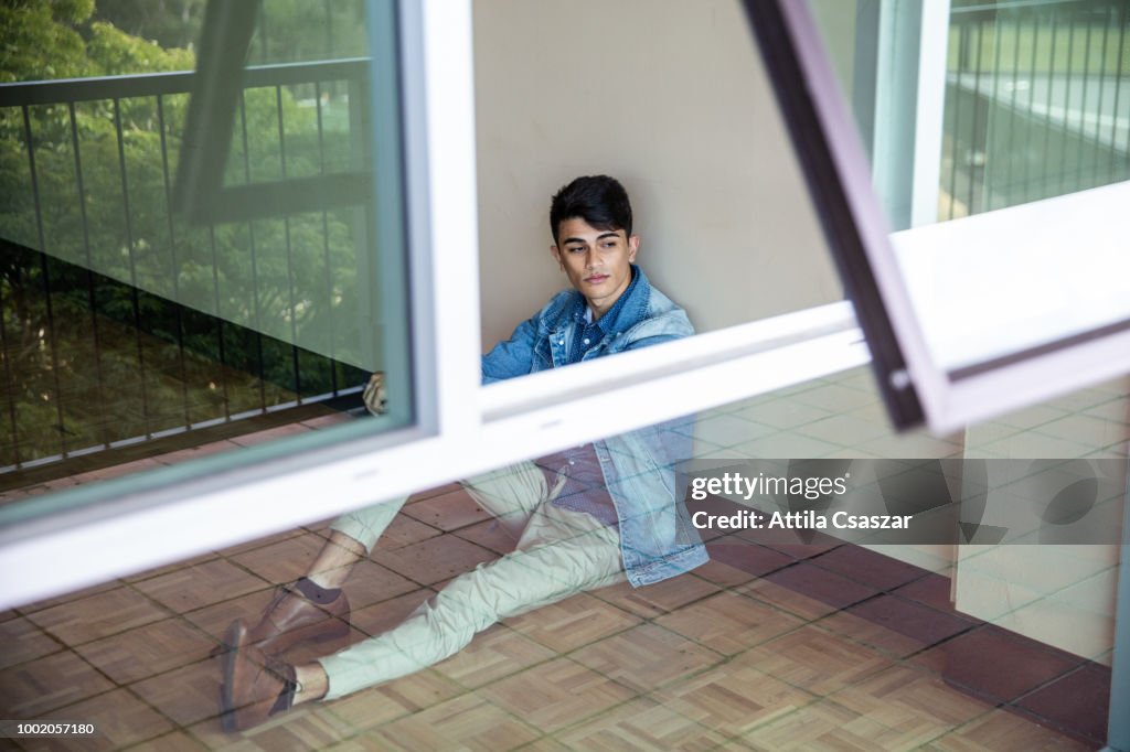 Portrait of a young man sitting at a wall and looking outside through window