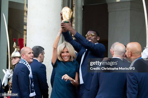 French President Emmanuel Macron's wife Brigitte Macron holds the trophy next to France's midfielder Paul Pogba at a reception for the French...