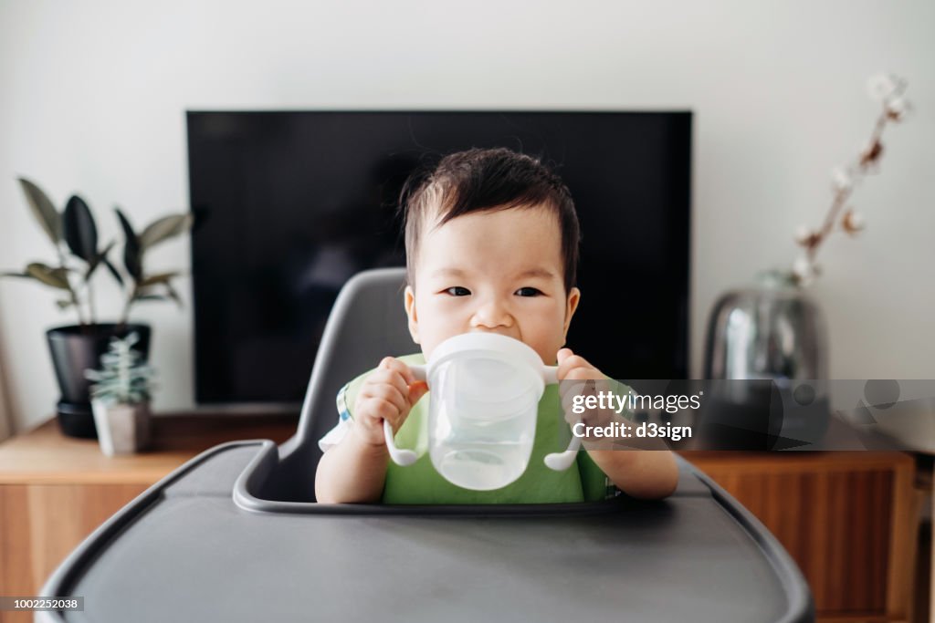 Cute baby drinking water from sip cup on high chair