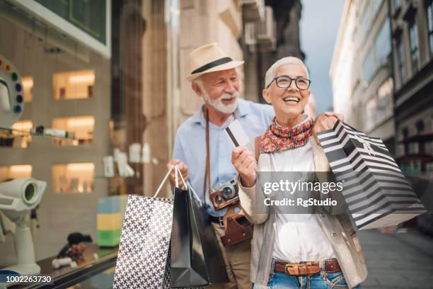 lächelnde paar holding einkaufstaschen und eine kreditkarte - geld ausgeben stock-fotos und bilder