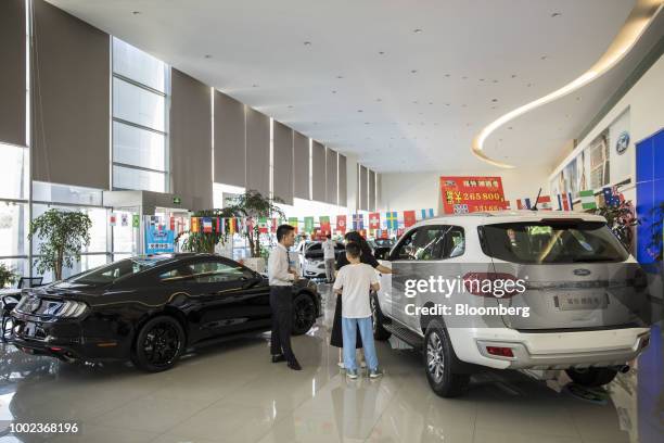 Customer speaks with a sales agent while standing between a Ford Motor Co. Everest sport utility vehicle , right, and a Mustang sports car on display...